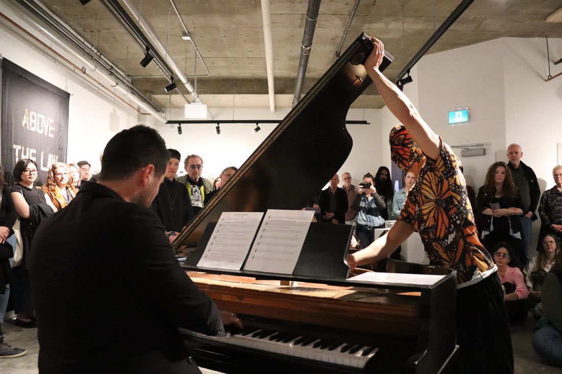 David Khang dressed as a monarch butterfly patterned wrestler, preparing to wrestle with a grand piano in front of a live audience.