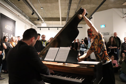 David Khang dressed as a monarch butterfly patterned wrestler, preparing to wrestle with a grand piano in front of a live audience.